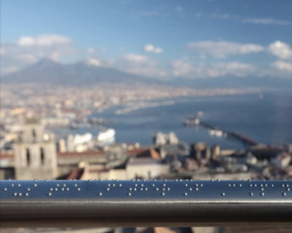 In primo piano l'installazione in braille, sullo sfondo sfocato del golfo di Napoli e Sorrento.